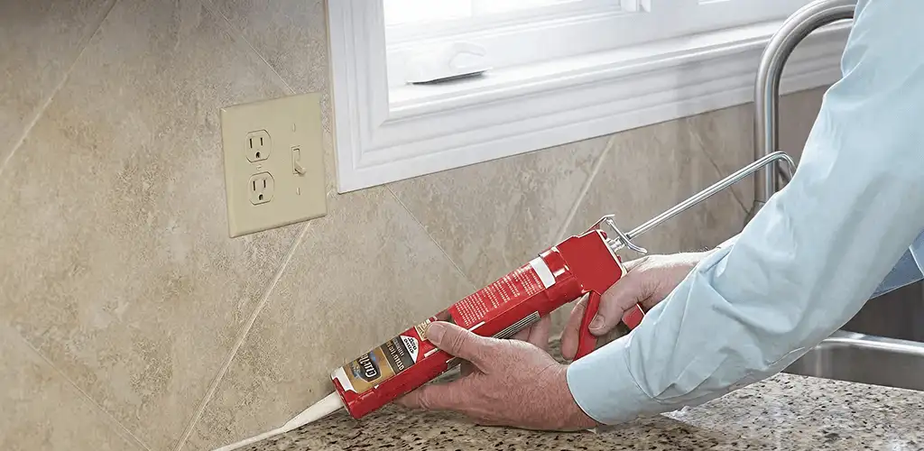 Handyman applying caulk along a kitchen backsplash and countertop seam in Wichita, KS