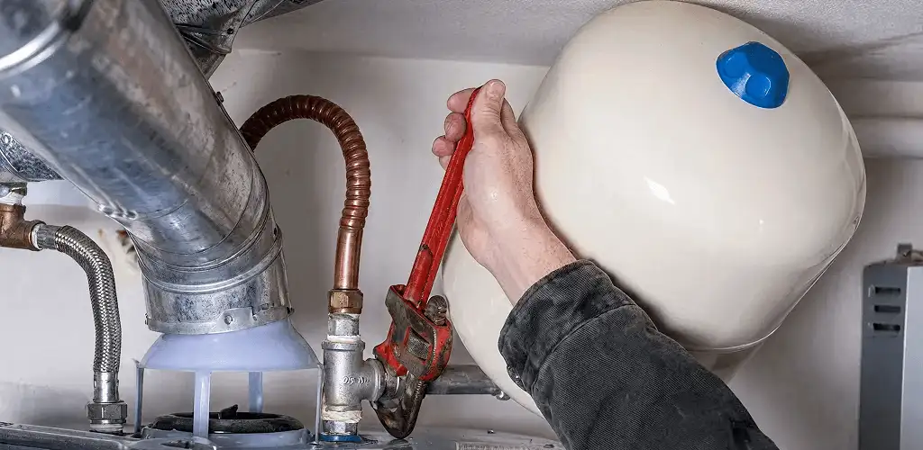 Water heater repair technician tightening plumbing connections near a tank unit in Wichita, KS